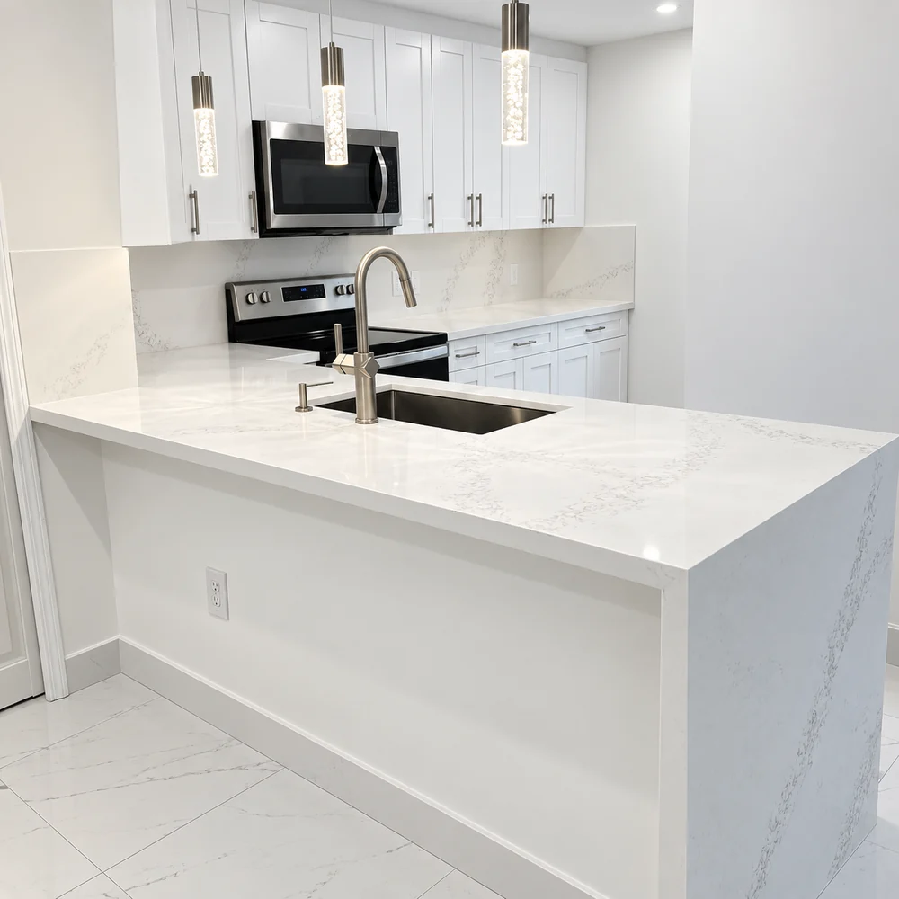 Cocina blanca en L con encimera de cuarzo, fregadero bajo encimera, electrodomésticos de acero y colgantes de cristal