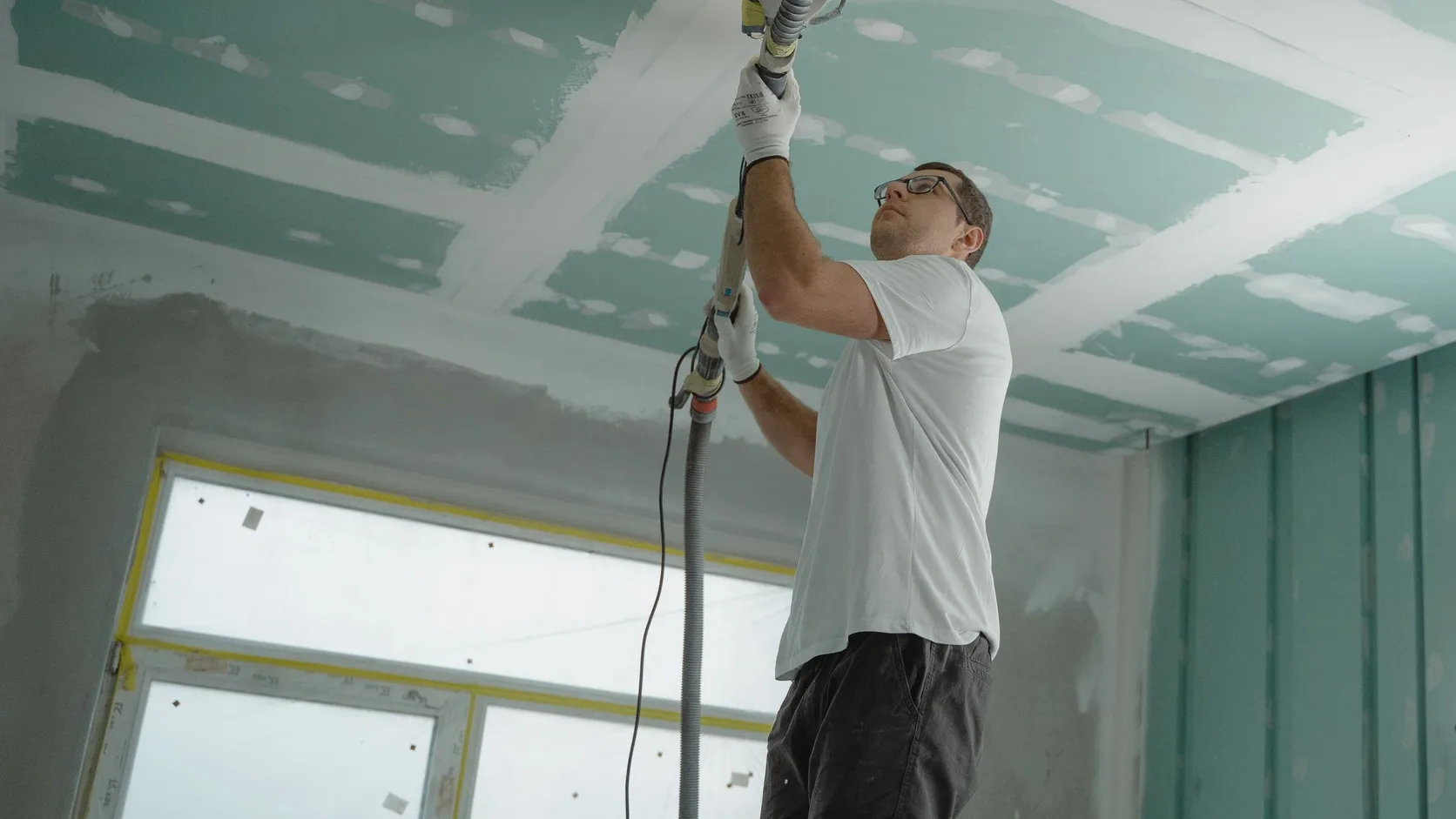 Operario lijando juntas de drywall en techo y muros antes del acabado.